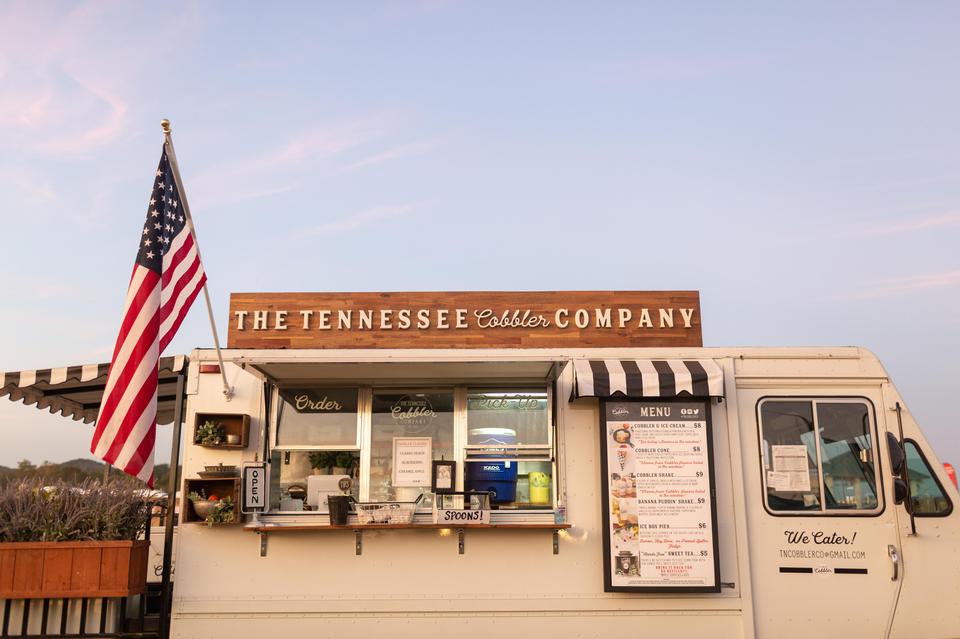 A food truck named "the tennessee cobbler company" under a clear sky with an american flag displayed on the left side.